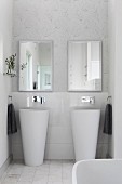 Twin designer pedestal sinks below mirrors on wall with delicate graphic pattern of leaves