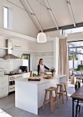 Young woman cooking in white open-plan kitchen with island counter and exposed beams in open roof area