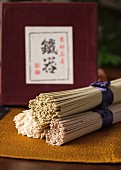 Three bundles of soba and udon noodles on a golden mat