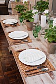 Table set with green crystal glasses, woven place mats and geraniums in terracotta pots