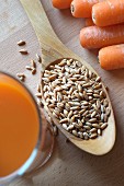 Spelt grains on a wooden spoon with carrots and carrot juice