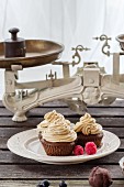 Chocolate cupcakes with butter cream and fresh berries on an old wooden table in front of a window
