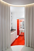 View through open curtain into modern kitchenette with orange floor and view into bathroom through open sliding door