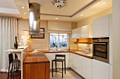 Designer Küche mit weissen Schrankfronten und Holz Arbeitsplatte, über Theke Edelstahl Dunstabzug integriert in Deckenfries mit Einbaustrahlern