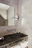 Shallow, trough-style sink with black patina in purist bathroom with concrete walls