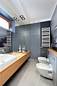 Elongated modern bathroom with long washstand below mirrored wall opposite toilet and bidet