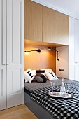 Double bed integrated in niche of fitted wardrobes, black and white bed linen and scatter cushions, glasses and carafe on tray