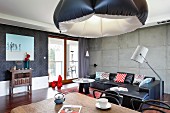 Eklektizistischer Stil in offenem Wohnraum mit aufgeblasenem Lampenschirm, schwarze Ledercouch vor Sichtbetonwand