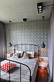 Black vintage metal bed flanked by pendant lamps against tiled wall with black and white floral pattern in bedroom