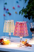 Brightly printed paper folded into concertinas as lampshades for tealights in stemmed glasses