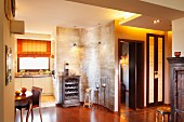 Silbern schimmernde, geschwungene Raumteilerwand mit Weinregal vor moderner Einbauküche, Essplatz mit Biedermeiertisch