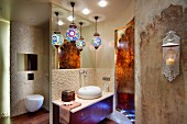 Colourful, patterned spherical lamps above washstand with pebble mosaic tiles, separate toilet and vintage Oriental-style wall design