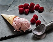 Raspberry ice cream in a cone next to fresh raspberries
