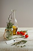 A bottle of olive oil, thyme and cherry tomatoes on a light wooden surface