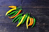 Various different coloured chilli peppers on a wooden surface