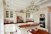 White country-house kitchen with dining area, counter and chandelier in grand interior