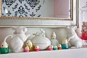 Osterdeko auf Kaminsims, Porzellan Tierfiguren in Weiß und bemalte Eier in Förmchen aus Glas und Papier