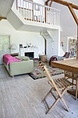 Holz Klappstuhl an teilweise sichtbarem Esstisch, im Hintergrund Loungebereich mit Sofa vor Kamin, in offenem Wohnraum