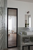 Bad mit Standspiegel neben Waschtisch mit silberfarbenen, glänzenden Mosaikfliesen