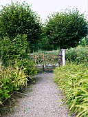 Gekiester Weg im Garten und Blick auf rustikales Gartentor