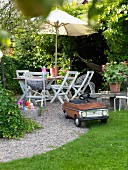Auto Spielzeug Gefährt im Retrostil auf Kiesweg, im Hintergrund idyllisches Gartenplätzchen mit Tisch und Stühlen unter Sonnenschirm