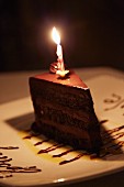 A slice of chocolate cake with a birthday candle