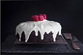 A Red Velvet cake with icing sugar and raspberries on a wire rack