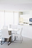 Dining table and open-plan kitchen area in white, elegant interior