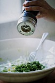 Hand mit Pfeffermühle mahlt Pfeffer über einen Salat