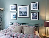 Black metal double bed with checked bed linen below framed black and white photos on pastel green wall
