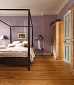 Modern wooden double bed with canopy frame in bedroom with mauve walls and rustic wooden floor