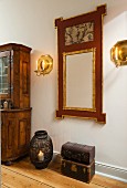 Stacked antique trunks, candle lantern on floor and mirror with carved gilt frame flanked by brass candle sconces