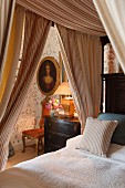 Antique portrait, antique chest of drawers, floral wallpaper and four-poster bed with striped curtains in foreground