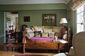 Antique daybed with wooden frame, many scatter cushions in traditional living room with green-painted walls