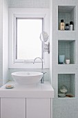 Modern washstand below window and fitted shelf niches with mosaic tiles in bright bathroom