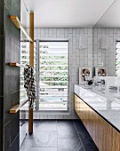 Fitted washstand and wooden towel rack in modern designer bathroom with charcoal-grey tiles