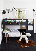 Children's bedroom in charcoal grey with colourful garland of pompoms on bunk beds and dog figurine on animal-skin rug