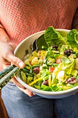 A woman holding a bowl of vegan Nicoise salad