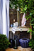 Improvised shower area in garden with wicker hurdle screen and blue planters on floor