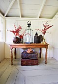 Kerzen-Laterne und Gefässe mit Zweigen auf Tropenholztisch, Vintage-Koffer auf dem weiss patinierten Holzboden