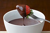 A strawberry being dipped into melted chocolate