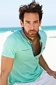 A young man on a beach wearing a light turquoise polo shirt