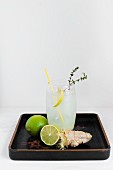 A glass of ginger and lime soda with ingredients on a varnished tray