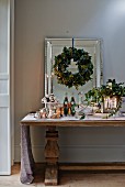 Festive arrangement for Christmas buffet on antique table below wreath of leaves on wall