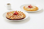 Round waffles and pancakes dusted with icing sugar and topped with strawberries