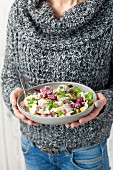A woman holding a bowl of beetroot and potato salad with ham and a creamy horseradish sauce