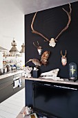 Hunting trophies and stuffed birds hung on black-painted wall next to floor-to-ceiling open doorway with view into kitchen