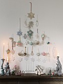 Pastel-coloured Christmas tree baubles hung in the shape of a Christmas tree over a chest of drawers with ceramic figurines