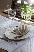 Place setting with decoratively folded linen napkin on white runner and flowers in drinking glass