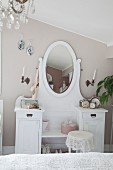 White dressing table with oval mirror against wall painted pastel grey in bedroom